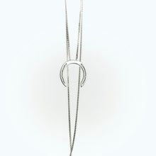 A delicate silver necklace with a horseshoe pendant, featuring small diamonds embedded in the design. The chain is elegantly draped, showing a clasp at the bottom, set against a light background.