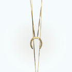 A delicate gold necklace with a horseshoe pendant, featuring small diamonds embedded in the holes, set against a light background.