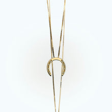 A delicate gold necklace with a horseshoe pendant, featuring small diamonds embedded in the holes, set against a light background.