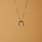 A delicate gold necklace with a horseshoe pendant, featuring small diamonds embedded in the holes, set against a light background.